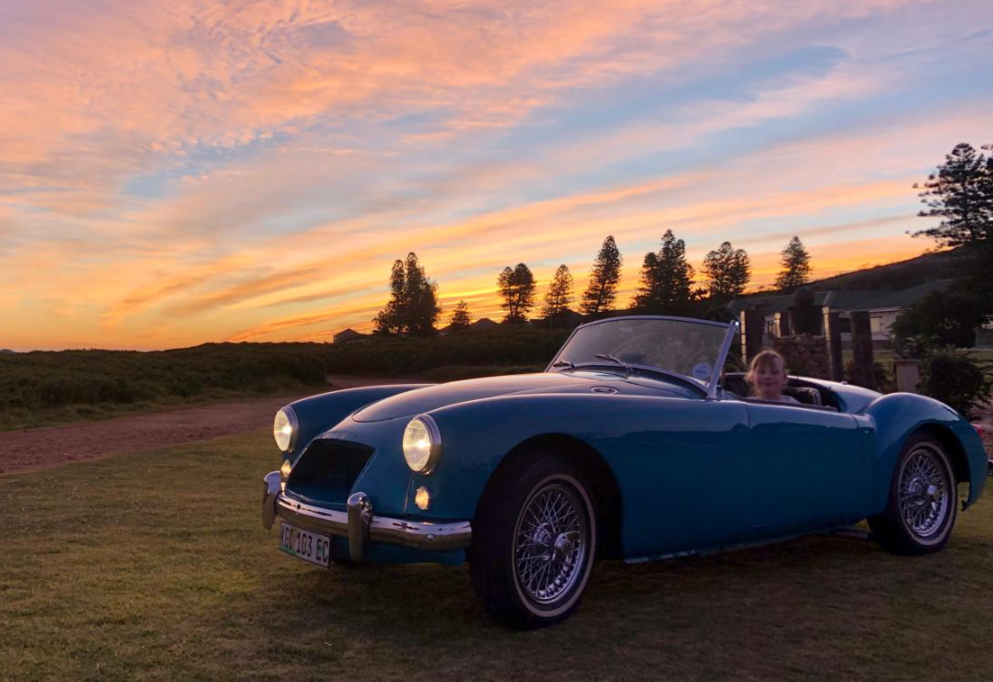 Flip's granddaughter sitting behind the wheel of the MGA at sunset